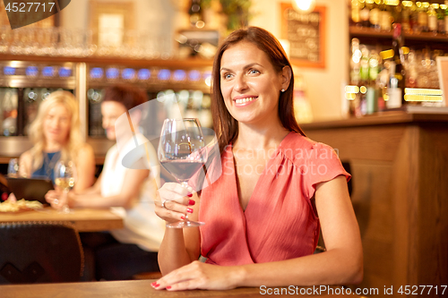 Image of happy woman drinking red wine at bar or restaurant