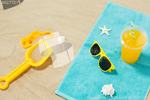 Image of sunglasses, sand toys and juice on beach towel