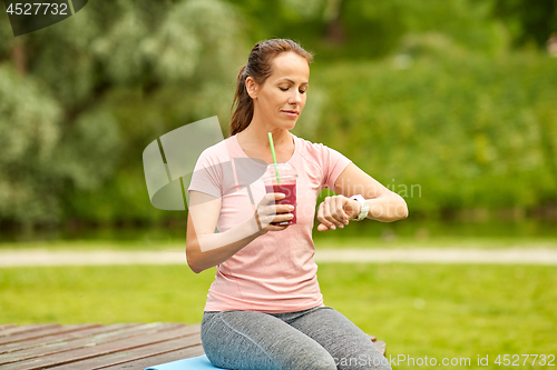 Image of woman with smoothie looking at smart watch in park