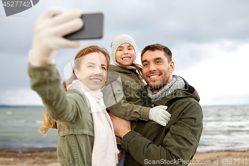 Image of family taking selfie by smartphone on autumn beach