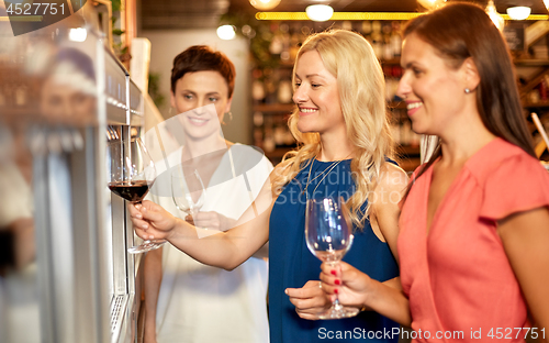 Image of happy women pouring wine from dispenser at bar