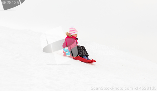 Image of happy little girl sliding down on sled in winter