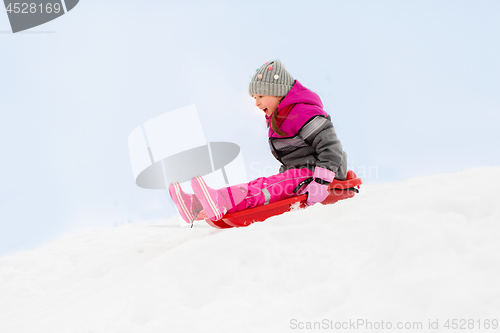 Image of happy little girl sliding down on sled in winter