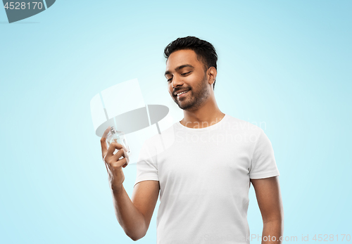 Image of happy indian man with perfume over blue background