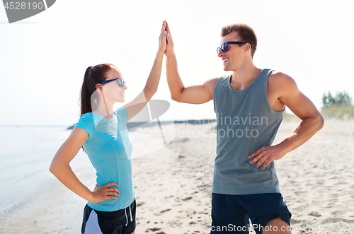 Image of happy couple in sports clothes and shades on beach