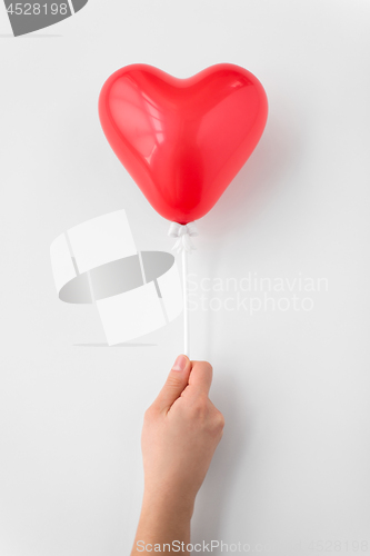 Image of close up of hand holding red heart shaped balloon