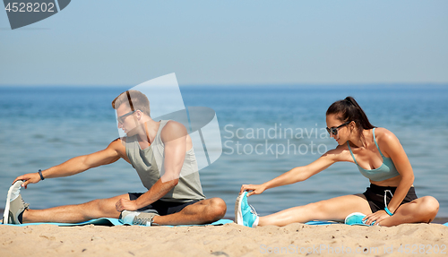 Image of happy couple stretching legs on beach