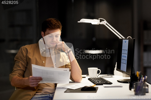 Image of designer with papers and computer at night office