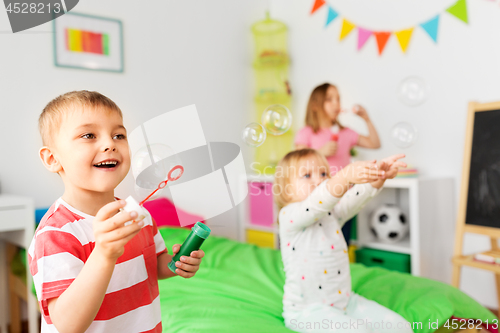 Image of happy children blowing soap bubbles at home