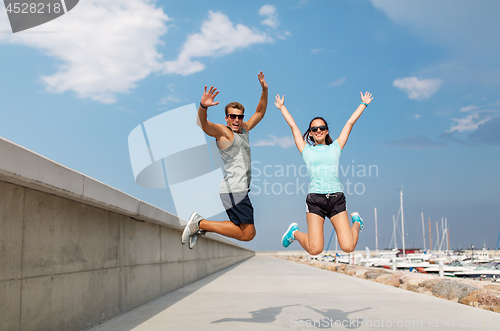 Image of happy couple in sports clothes jumping on pier