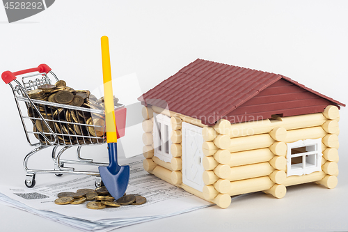 Image of A trolley with money in the bills for an apartment, a shovel stands next to it, a toy house is near