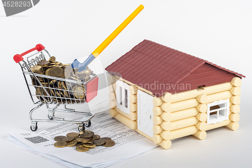 Image of A trolley with money in the bills for an apartment, a shovel stuck in a trolley, a toy house next to it