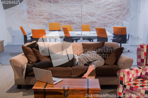 Image of man sleeping on a sofa  in a creative office