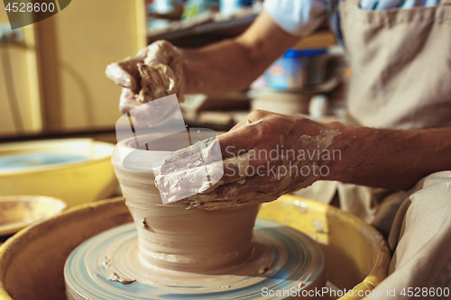 Image of Creating a jar or vase of white clay close-up. Master crock. Man hands making clay jug macro.