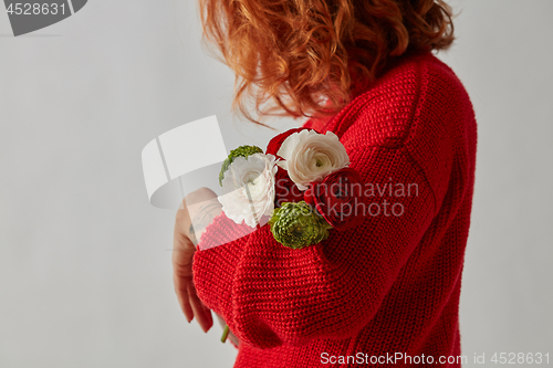 Image of Young red-haired woman with tender flowers of a Ranunculus on a gray background with copy space. Greeting card layout