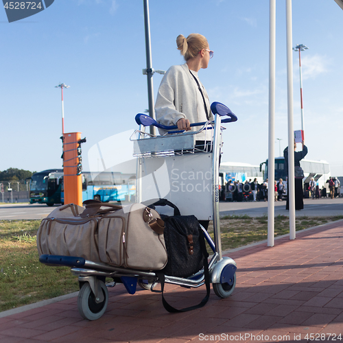 Image of Young woman transporting luggage from arrival parking to international airport departure termainal by luggage trolley.