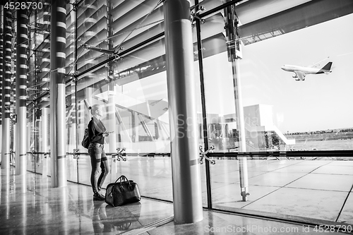 Image of Young woman waiting at airport, looking through the gate window.