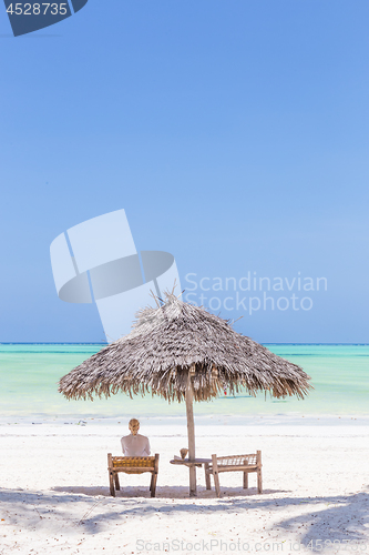 Image of Women relaxing on dack chair under wooden umbrella on tropical beach.