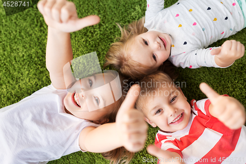 Image of happy kids lying on floor and showing thumbs up