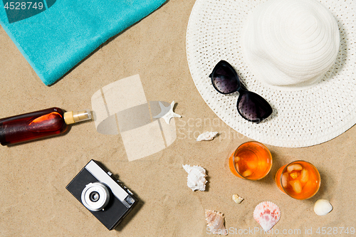 Image of drinks, hat, camera and sunglasses on beach sand