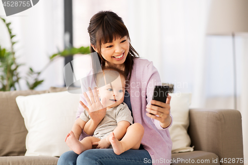 Image of asian mother with baby son taking selfie at home