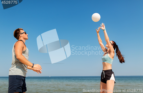 Image of happy couple playing volleyball on summer beach