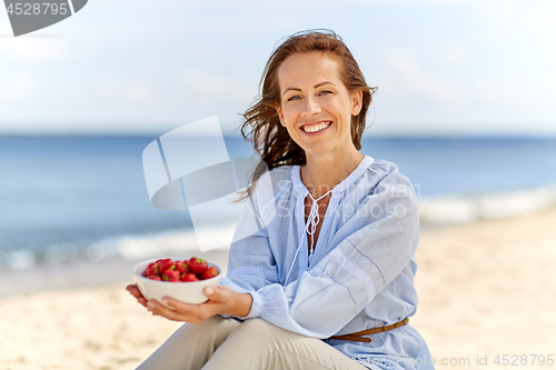 Image of woman holding bowl with strawberries on beach