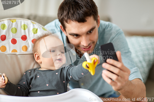 Image of father with baby daughter taking selfie at home