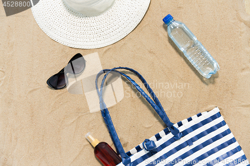 Image of beach bag, sunscreen, sunglasses and hat on sand
