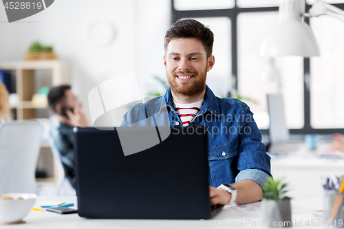 Image of smiling creative man with laptop working at office