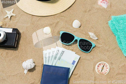 Image of money in passport, shades and hat on beach sand