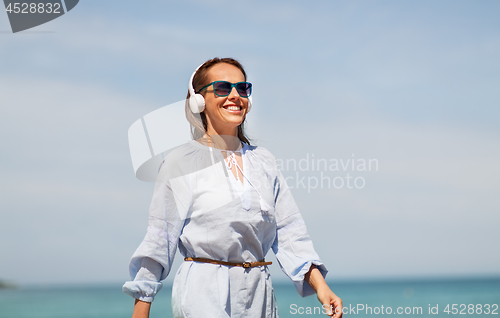 Image of woman with headphones walking along summer beach