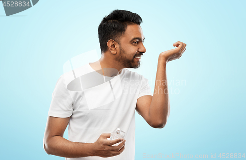 Image of happy indian man with perfume over blue background