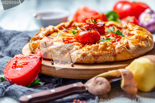 Image of Open pie with potatoes, bacon, onions and tomatoes.