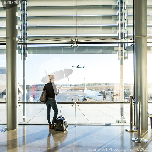 Image of Young woman waiting at airport, looking through the gate window.