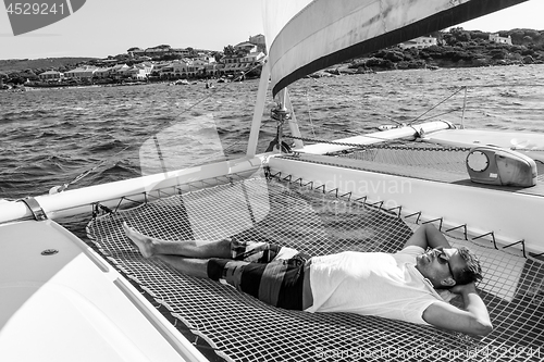 Image of Sporty man relaxing on a luxury catamaran sailing boat.