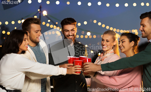 Image of friends clinking party cups on rooftop at night