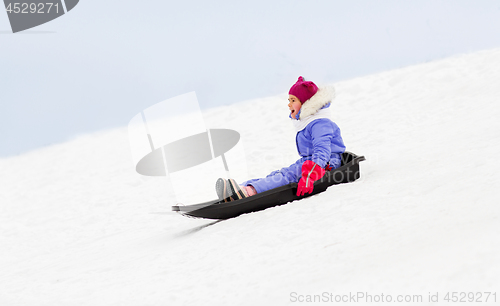 Image of happy little girl sliding down on sled in winter