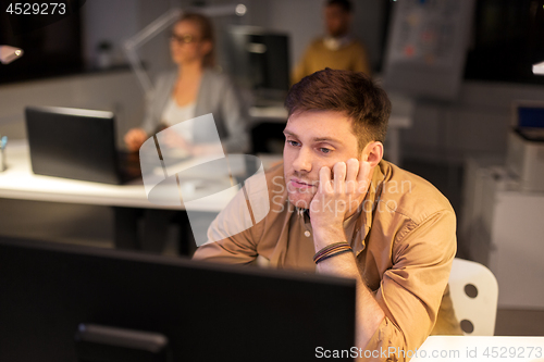 Image of tired or bored man with computer at night office