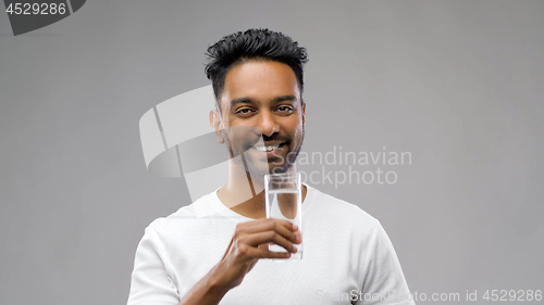 Image of happy young indian man drinking water from glass