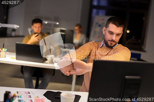 Image of man working late at night office and stretching