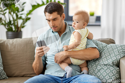 Image of father with baby daughter using smartphone at home