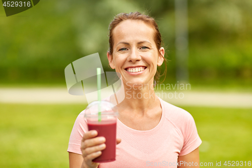 Image of woman drinking smoothie after exercising in park