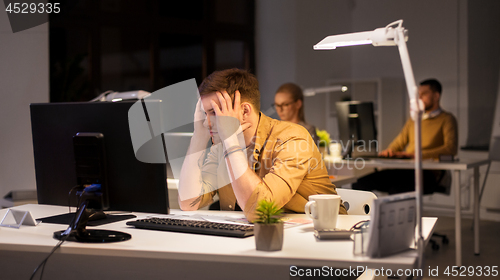 Image of stressed man at computer monitor at night office