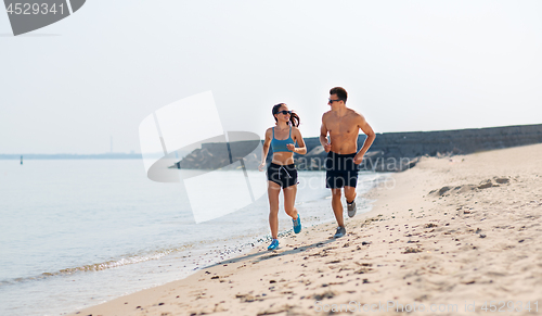 Image of couple in sports clothes running along on beach