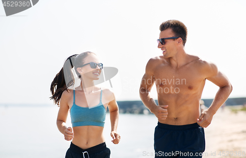 Image of couple in sports clothes running along on beach
