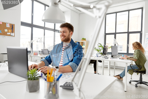 Image of smiling creative man with laptop working at office