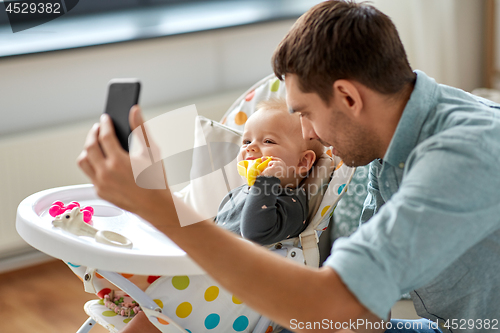 Image of father with baby daughter taking selfie at home