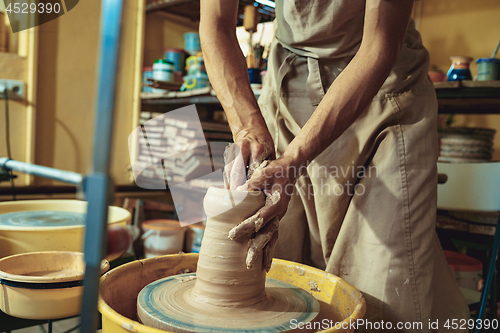 Image of Creating a jar or vase of white clay close-up. Master crock. Man hands making clay jug macro.