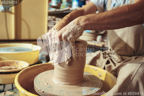 Image of Creating a jar or vase of white clay close-up. Master crock. Man hands making clay jug macro.